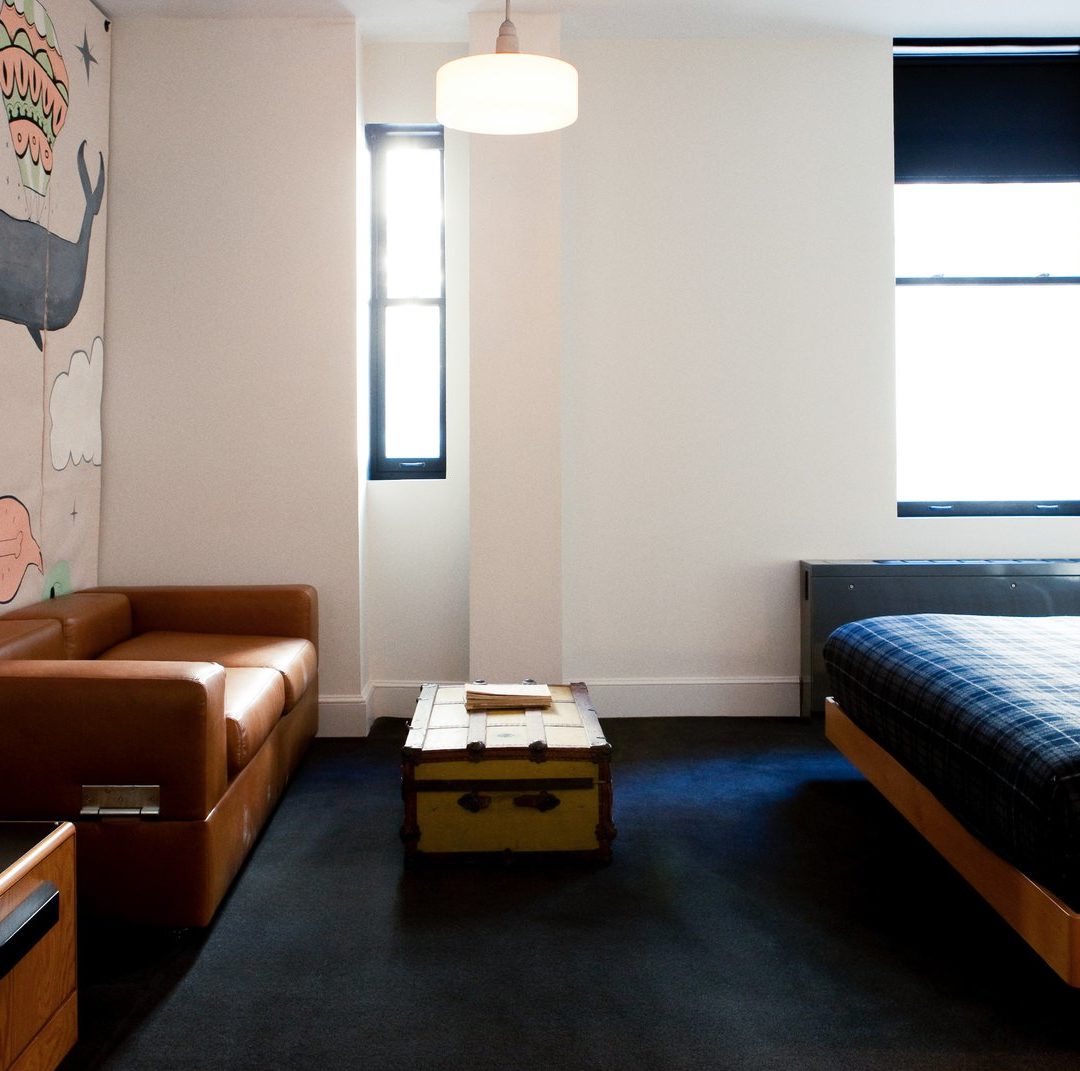 A room with dark carpets features two windows and a brown leather sofa